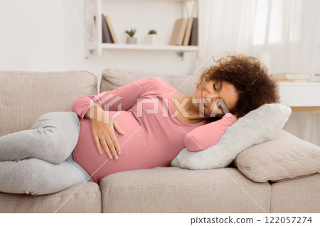Happy afro pregnant woman napping on sofa, having sweet day dream and smiling, free space Happy afro pregnant woman napping on sofa, having sweet day dream and smiling, free space 122057274
