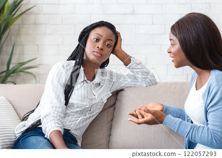 Indifference in friendship. Bored black girl tired of listening her talkative girlfriend while sitting on sofa at home together 122057293