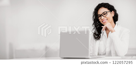 Business Concept. Happy mexican woman using laptop, watching movie, working in modern office, copyspace 122057295