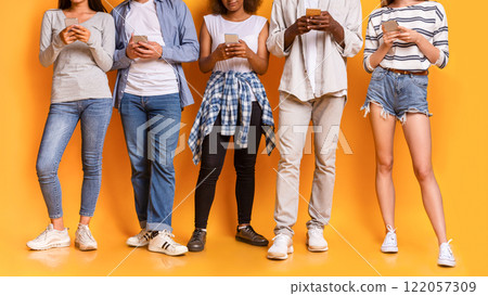 Teenaged international group of friends using smartphones, cropped, yellow studio background Teenaged international group of friends using smartphones, cropped, yellow studio background 122057309