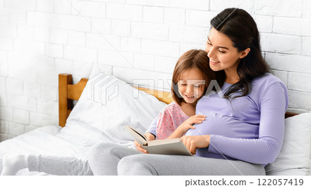 Loving pregnant mom reading book to her little daughter while resting together in bed, copy space Loving pregnant mom reading book to her little daughter while resting together in bed, copy space 122057419