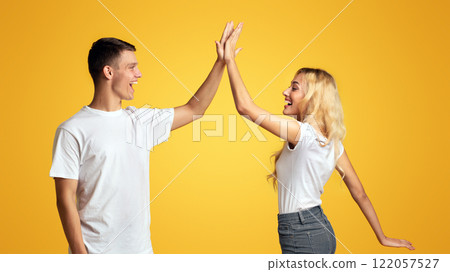 Joyful Millennial Guy And Girl Greeting Each Other With High Five, Clapping Hands Over Yellow Background 122057527