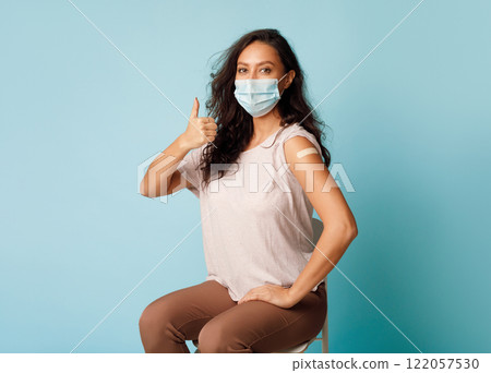 Covid-19 Vaccination. Vaccinated Woman Gesturing Thumbs Up Showing Arm With Plaster Bandage After Coronavirus Vaccine Injection On Blue Background, Wearing Protective Face Mask. Antivital Immunization 122057530