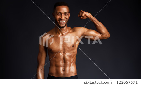 Athletic Man's Torso. Happy afro fitness model showing shoulder muscles, strong hands, chest and biceps over black wall 122057571