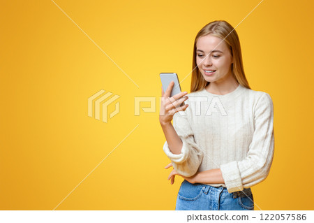 Nice App. Beautiful teen girl holding and using smartphone over orange studio background, copy space 122057586