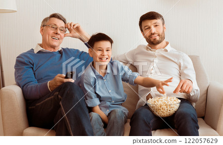 Grandfather, Father And Son Watching TV Switching Channels Sitting On Sofa At Home. Family Movies. Selective Focus Grandfather, Father And Son Watching TV Switching Channels Sitting On Sofa At Home. Family Movies. Selective Focus 122057629