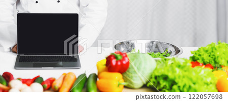 Unrecognizable Chef Man Showing Laptop Blank Screen Standing Next To Work Table With Groceries And Vegetables Cooking In Kitchen. Mockup 122057698