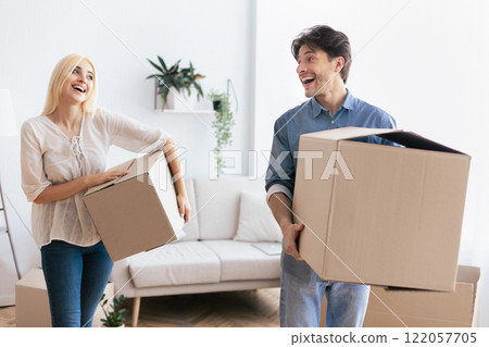A couple happily carries boxes into their new home, smiling and laughing together. 122057705