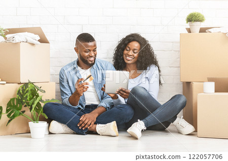 Furniture stores online. African girl showing her man ideas for interior in new house, using digital tablet, guy holding credit card, copy space 122057706