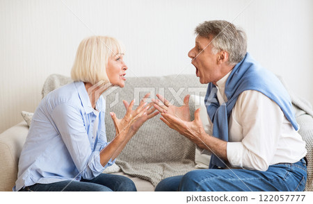 Senior couple quarrelling with each other and shouting, sitting on sofa at home Senior couple quarrelling with each other and shouting, sitting on sofa at home 122057777