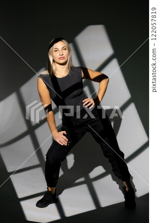Dancer posing in studio with window light shadows, wearing black clothes Dancer posing in studio with window light shadows, wearing black clothes 122057819