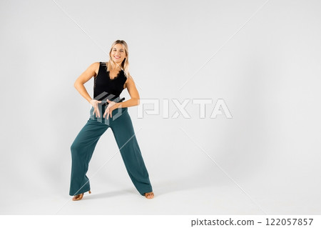 Young blonde dancer posing with hands joined and legs apart on white background 122057857