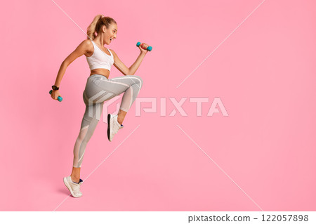 Fitness Lifestyle. Excited Girl Jumping Holding Dumbbells Exercising In Studio Over Yellow Background. Full Length Fitness Lifestyle. Excited Girl Jumping Holding Dumbbells Exercising In Studio Over Yellow Background. Full Length 122057898