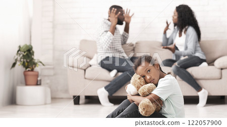 Family problems. Little black girl suffering from parents quarrels, sitting on floor cuddling her teddy bear, feeling lonely and depressed Family problems. Little black girl suffering from parents quarrels, sitting on floor cuddling her teddy bear, feeling lonely and depressed 122057900