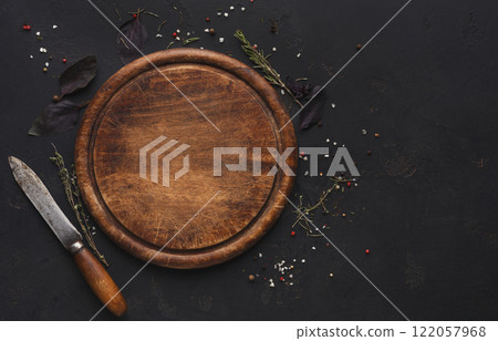 Wooden cutting board with knife and spices on dark background. Rustic catering platter for cutting pizza, bread or meals serving, top view Wooden cutting board with knife and spices on dark background. Rustic catering platter for cutting pizza, bread or meals serving, top view 122057968