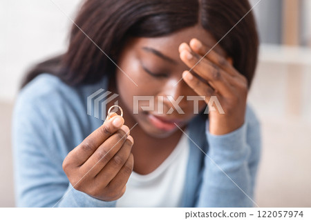 Divorce concept. Desperate heartbroken african american woman holding wedding ring, feeling depressed about ruined marriage and breaking up, closeup 122057974