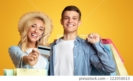 Happy customers. Joyful young couple recommending credit card, holding shopping bags and smiling on yellow background Happy customers. Joyful young couple recommending credit card, holding shopping bags and smiling on yellow background 122058013