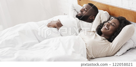 Young african american couple relaxing in bed after make love, lying with hands behind head and closed eyes. 122058021