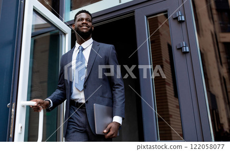 Young african american entrepreneur man leaving business center building after work, looking away and smiling, copy space. Business people and successful career concept Young african american entrepreneur man leaving business center building after work, looking away and smiling, copy space. Business people and successful career concept 122058077