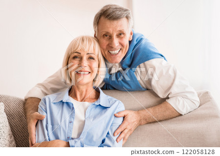 Lovely mature man embracing wife and smiling together to camera, resting at home Lovely mature man embracing wife and smiling together to camera, resting at home 122058128