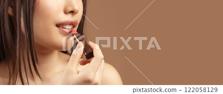 Cropped of unrecognizable asian lady using colorful lipstick over brown studio background, copy space. Lipstick, lipbalm, beauty products for lips, makeup concept 122058129