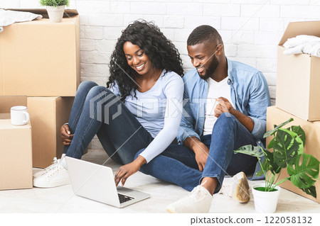 Cheerful african couple sitting on floor at new apartment, choosing new furniture online, using laptop, empty space Cheerful african couple sitting on floor at new apartment, choosing new furniture online, using laptop, empty space 122058132