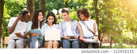 Learning Concept. Group Of College Friends With Laptop Preparing For Lessons Together, Sitting On Bench In Campus 122058135