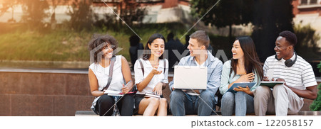 Campus Life. Cheerful college students resting outdoors between classes, using laptop, chatting and laughing, free space Campus Life. Cheerful college students resting outdoors between classes, using laptop, chatting and laughing, free space 122058157