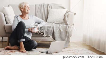 Cheerful elderly business lady sitting on floor at home, drinking coffee, using laptop, free space 122058302