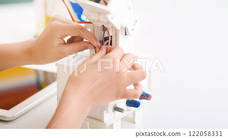 A close-up image of two hands working on a robotic toy kit, the hands are gently attaching a small copper wire to the robots assembly, copy space 122058331