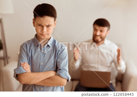 Angry Father Yelling At Offended Boy Working On Laptop Sitting On Couch At Home. Selective Focus Angry Father Yelling At Offended Boy Working On Laptop Sitting On Couch At Home. Selective Focus 122058443