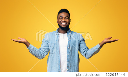 Make best decision. Black smiling guy making scales with his empty hands, comparing options over yellow studio background, panorama 122058444