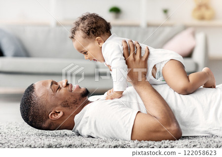 Father's Love. Happy Young Black Dad Bonding With Adorable Newborn Baby At Home, African American Man Playing With His Cute Infant Son On Floor In Living Room, Enjoying Spending Time Together Father's Love. Happy Young Black Dad Bonding With Adorable Newborn Baby At Home, African American Man Playing With His Cute Infant Son On Floor In Living Room, Enjoying Spending Time Together 122058623