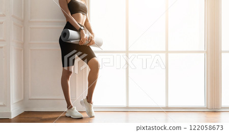 Ready For Training. Closeup cropped view of unrecognizable fit woman going to gym, holding and carrying roll mat standing by window in fitness studio or living room, free empty space, panorama Ready For Training. Closeup cropped view of unrecognizable fit woman going to gym, holding and carrying roll mat standing by window in fitness studio or living room, free empty space, panorama 122058673