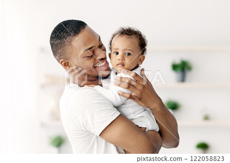 Father And Child. Happy Young Black Dad Embracing Cute Little Baby Boy While They Posing Together In Home Interior, Loving African American Daddy Looking At His Child And Smiling, Copy Space Father And Child. Happy Young Black Dad Embracing Cute Little Baby Boy While They Posing Together In Home Interior, Loving African American Daddy Looking At His Child And Smiling, Copy Space 122058823