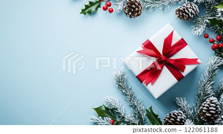 A white gift box with a red ribbon sits in the bottom right corner of a blue background, decorated with spruce branches and cones 122061188