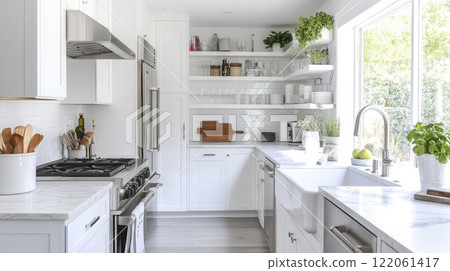 A white kitchen with stainless steel appliances, open shelving, and a farmhouse sink. The counter is white marble and the floor is a light wood. There are plants in the window and on the shelves. 122061417