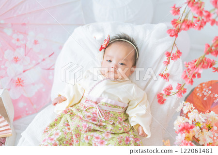 一個穿著紅色袴的可愛女嬰,在第一個節日的 Hinamatsuri 被春天的櫻花包圍著,看起來很開心 一個穿著紅色袴的可愛女嬰,在第一個節日的 Hinamatsuri 被春天的櫻花包圍著,看起來很開心 122061481