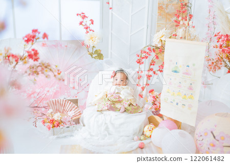 一個穿著紅色袴的可愛女嬰，在第一個節日的 Hinamatsuri 被春天的櫻花包圍著，看起來很開心 122061482