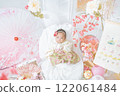 A cute girl baby in a red hakama who looks happy surrounded by spring cherry blossoms at the Hinamatsuri of the first festival 122061484