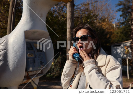 A Surprised Woman Joyfully Using a Quirky and Brightly Colored Phone Booth in a City Park 122061731