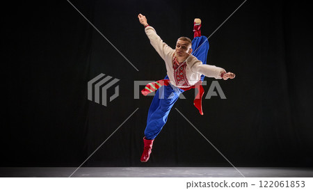 Male dancer in traditional Ukrainian attire, performing dance moves, showcasing strength and acrobatics of Hopak, against black studio background. 122061853