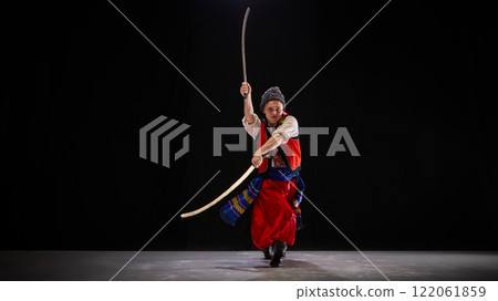 Dancer in Ukrainian folk outfit, confidently wielding dual swords in traditional Hopak stance, embodying historical spirit on dark background. Dancer in Ukrainian folk outfit, confidently wielding dual swords in traditional Hopak stance, embodying historical spirit on dark background. 122061859