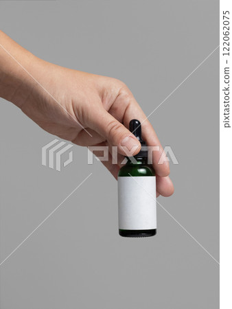 Hand holding dropper bottle with blank label against grey close up, cosmetic mockup 122062075