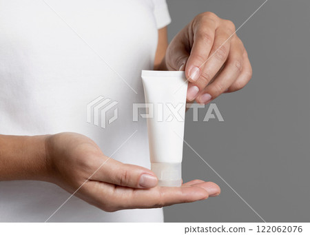 Female hands holding cream tube against white shirt close up, cosmetic mockup, copy space Female hands holding cream tube against white shirt close up, cosmetic mockup, copy space 122062076