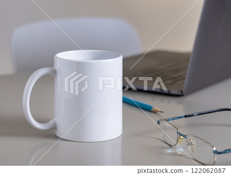 White coffee mug on grey office table against laptop, glasses and pencil closeup, mockup White coffee mug on grey office table against laptop, glasses and pencil closeup, mockup 122062087