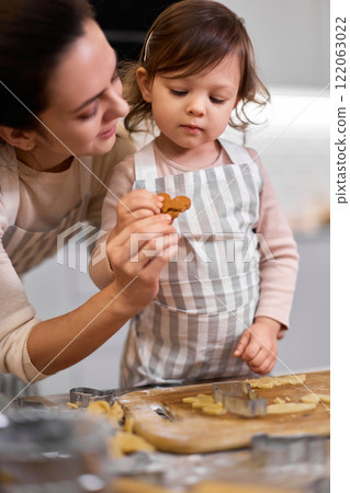 Happy family mother and little child daughter cutting cookies of raw gingerbread dough in kitchen 122063022