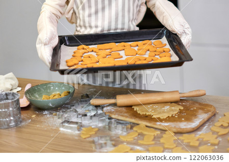 housewife woman in apron holds cookies on baking tray in kitchen 122063036