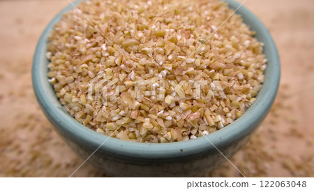 Broken Crushed Wheat (Dalia) in a Blue Bowl Isolated on Wooden Background Broken Crushed Wheat (Dalia) in a Blue Bowl Isolated on Wooden Background 122063048