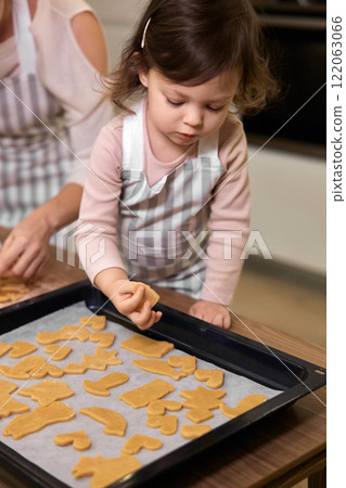 cute little girl putting gingerbread cookies on baking tray and helping mom bake cookies in kitchen, Christmas traditions 122063066